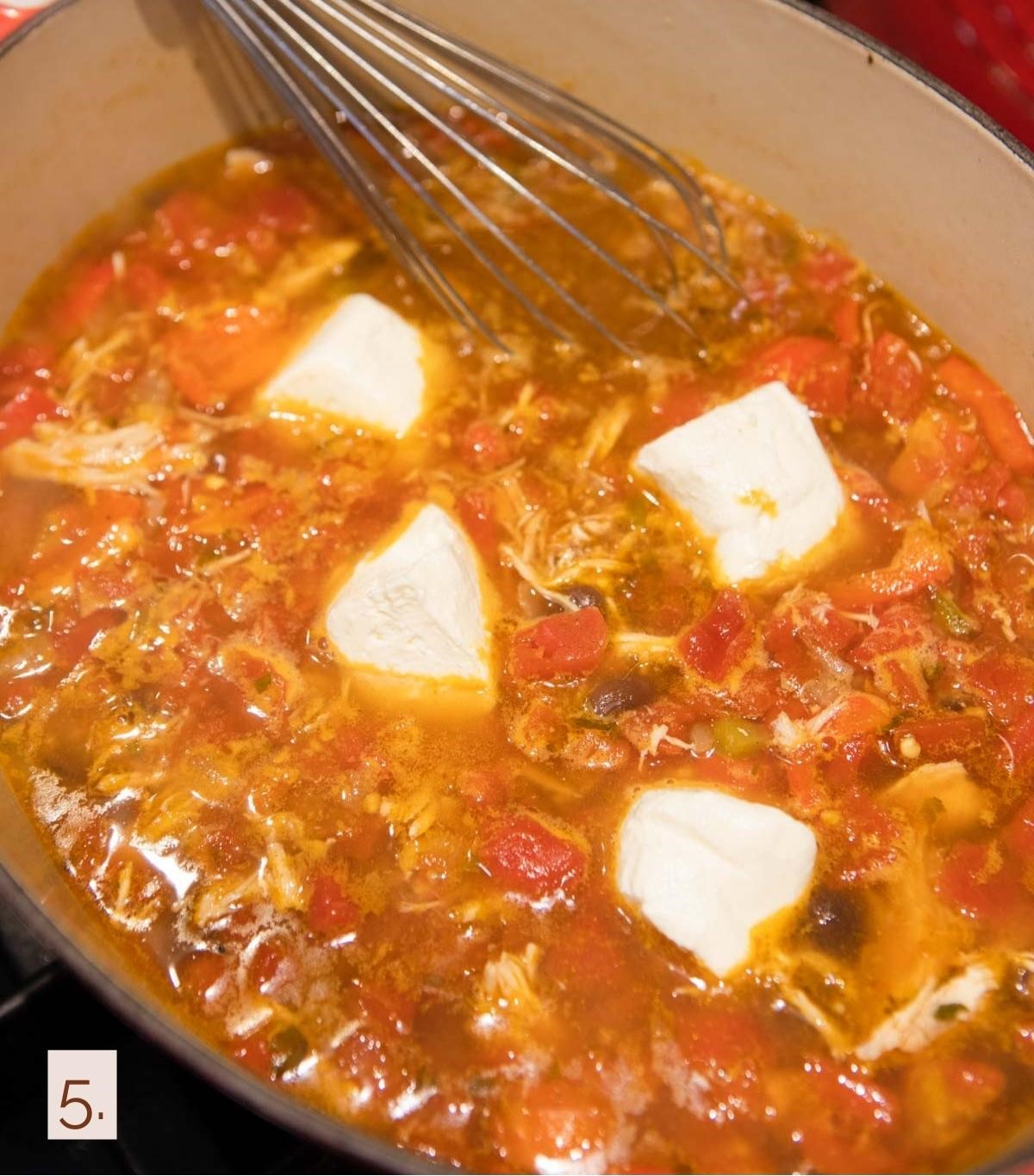 cream cheese being whisked into a dutch oven filled with chicken taco soup