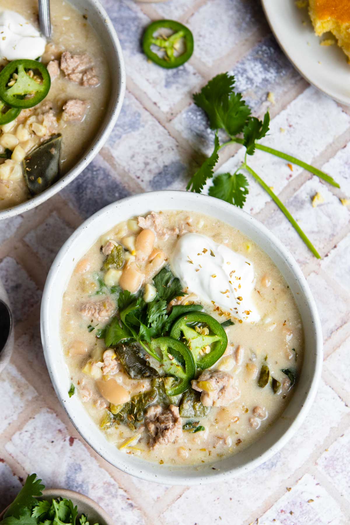 2 white bowl filled with white chicken chili Instant Pot and garnished with cilantro, jalapenos and sour cream