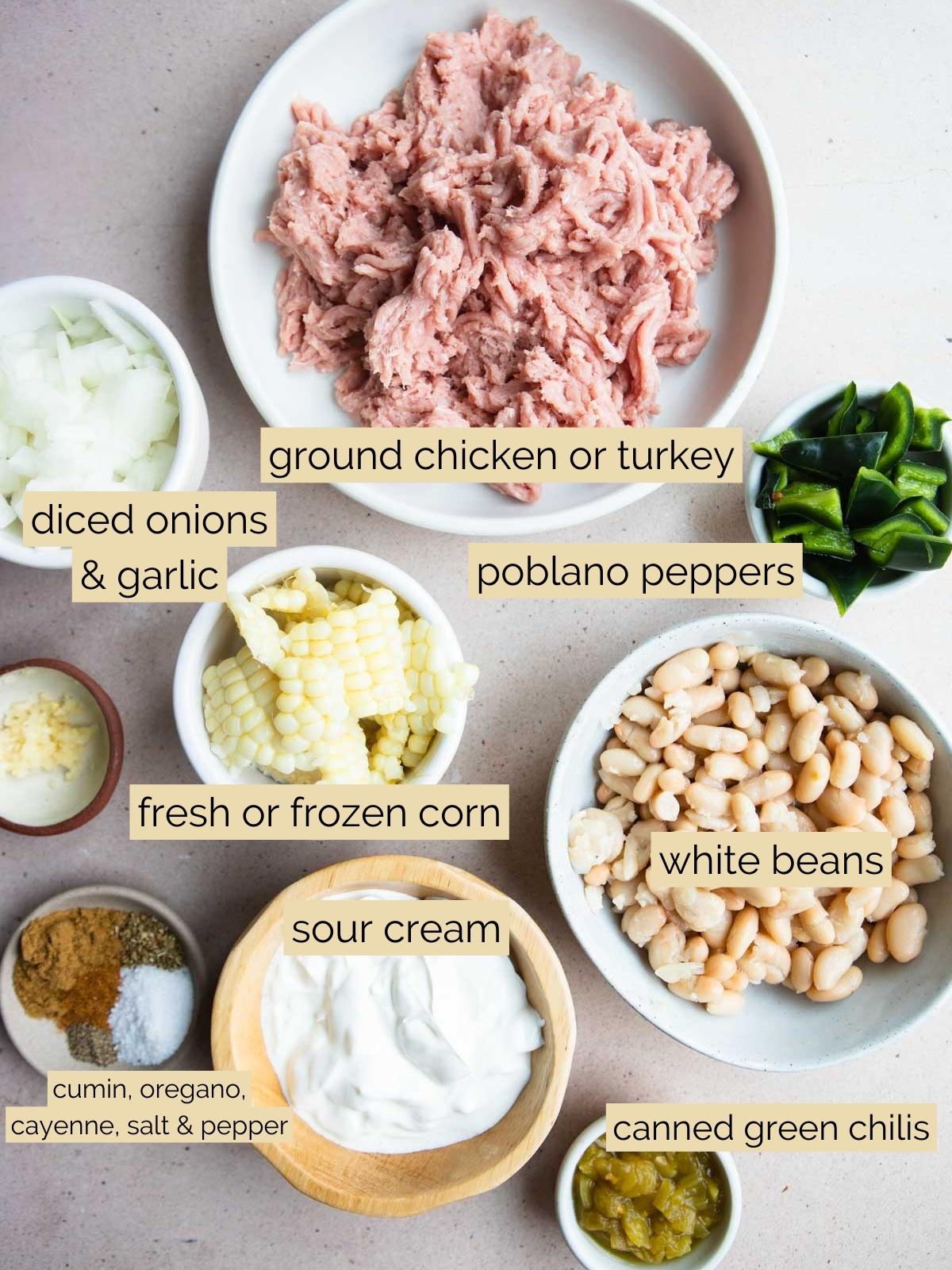 ingredients to make white chicken chili in small bowls on a beige surface