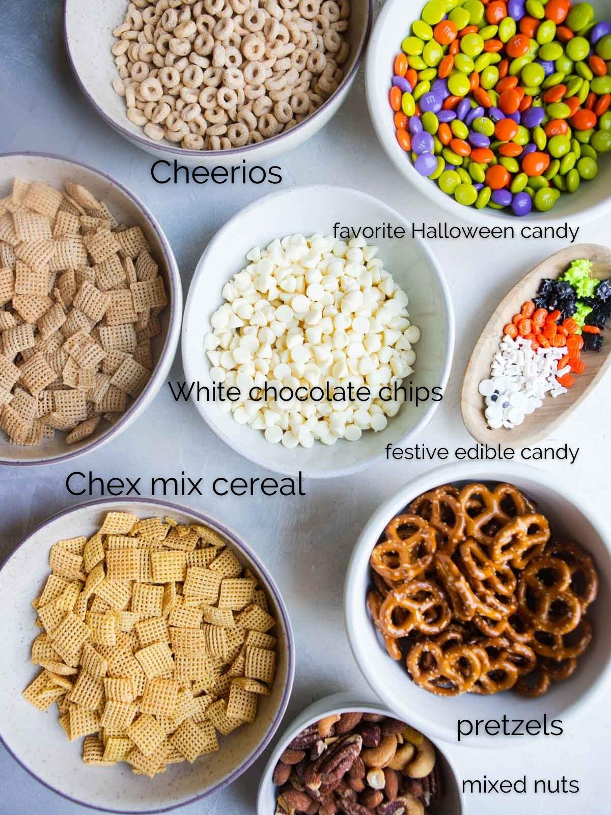 Halloween m&m's, Chex cereal, Cheerios cereal, mixed buts and white chocolate chips in small bowls