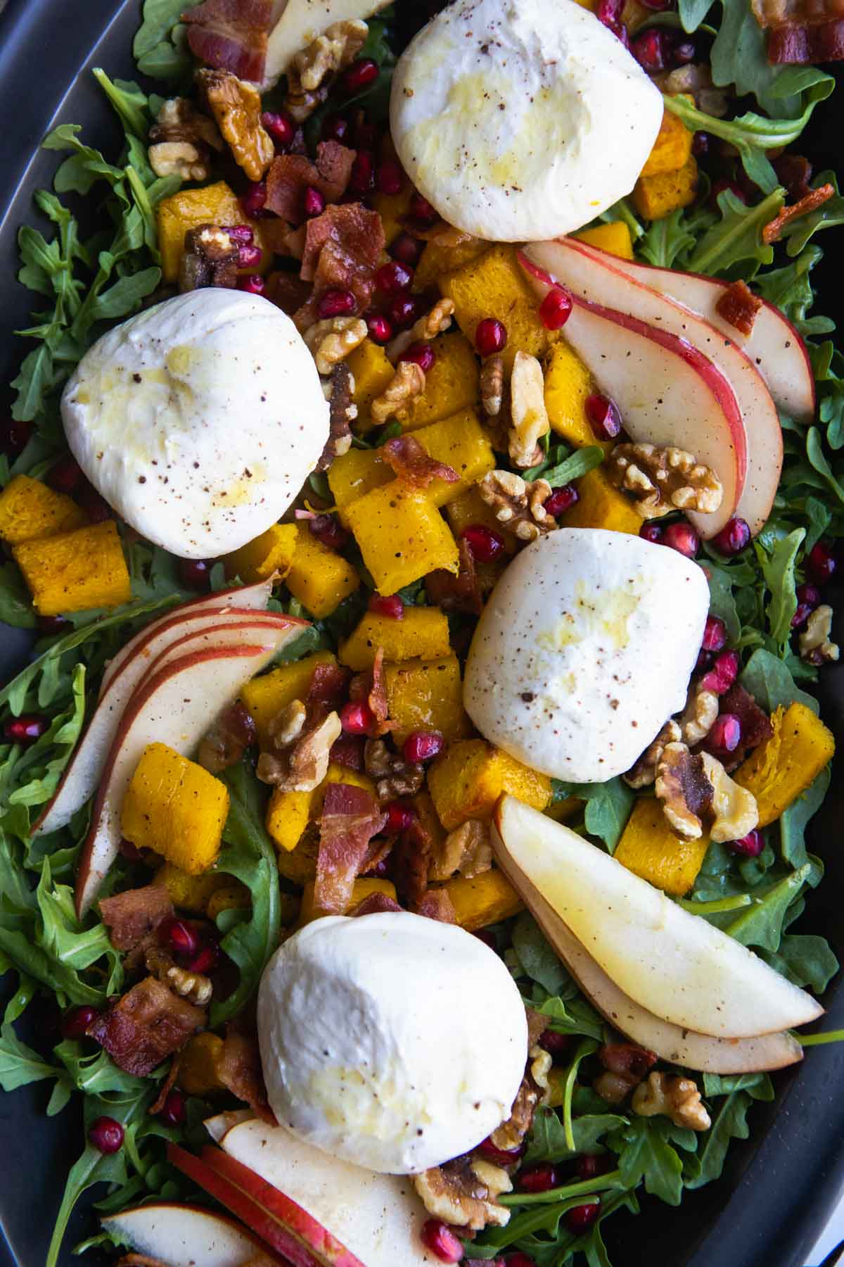 roasted pumpkin salad with walnuts, bacon, pomegranate seeds and burrata cheese served on a black platter
