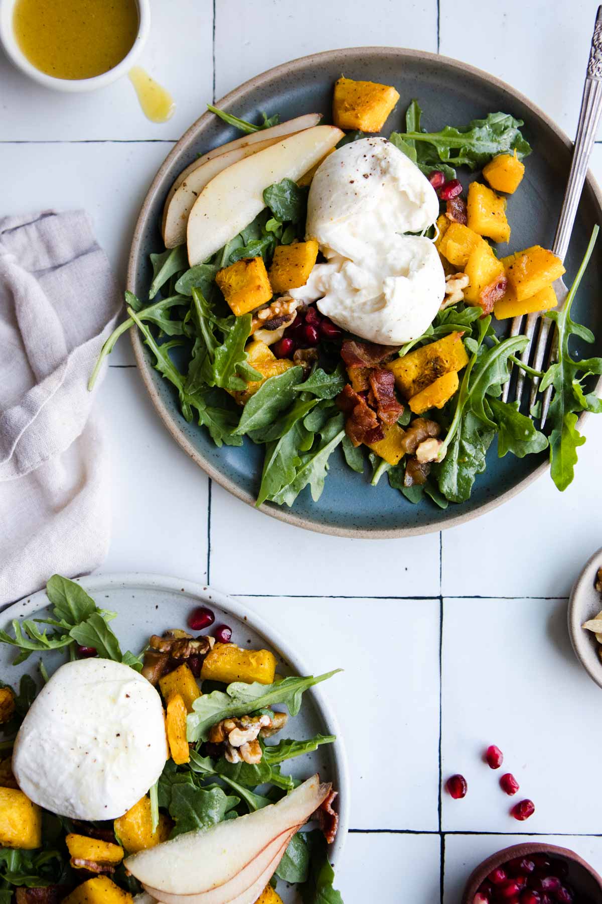 2 green plates served with a arugula salad topped with roasted pumpkin, pomegranate and burrata cheese 