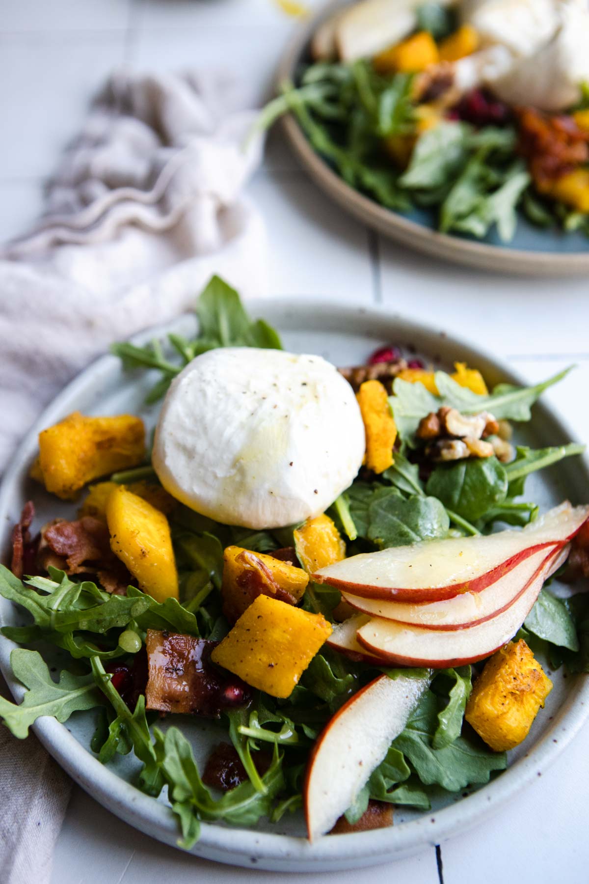 green plate filled with arugula, cubed and cooked pumpkin squash, sliced pear, bacon and burrata cheese