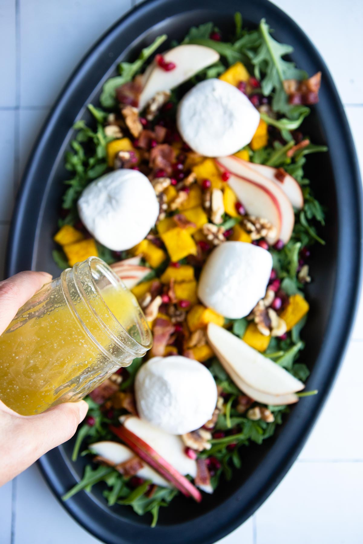 white balsamic vinaigrette being poured on a roasted pumpkin salad served on a black platter