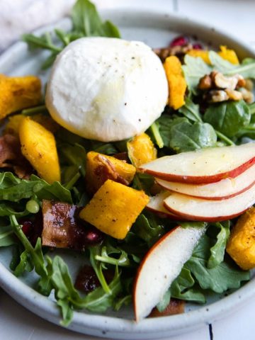 gray plate filled with roasted pumpkin salad and topped with bacon and burrata cheese, pear and pomegranate seeds