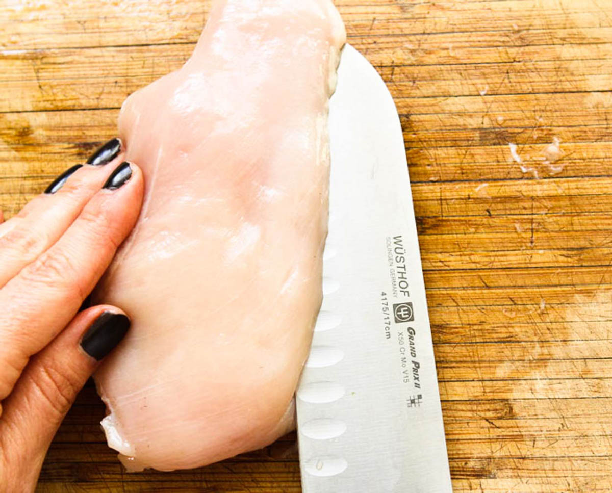 woman slicing a large chicken breast in half to make a thin chicken cutlet 