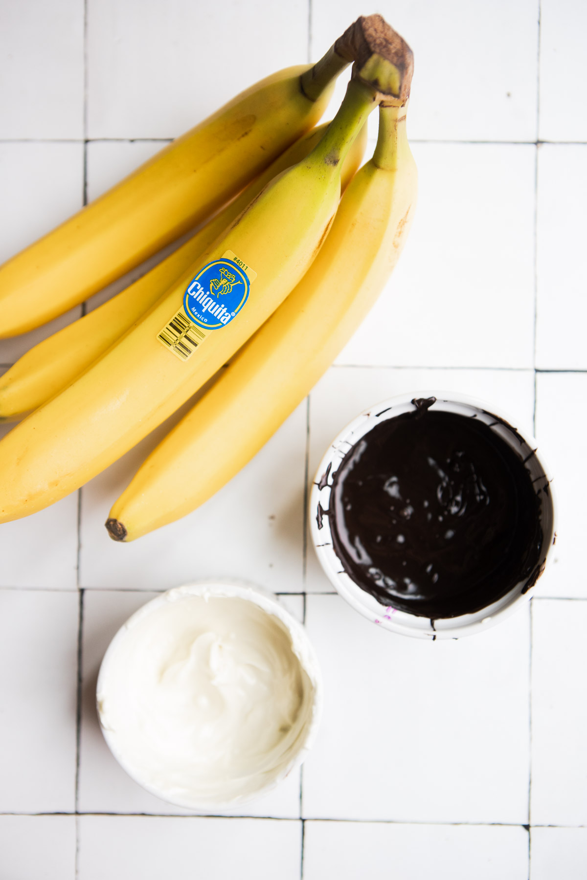 bananas with peel on, melted white chocolate and melted dark chocolate in small white bowls