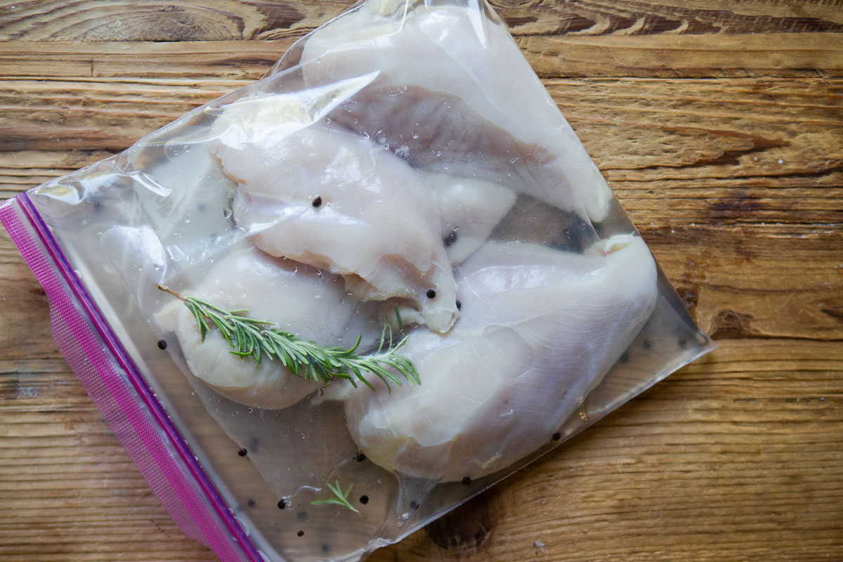 chicken breasts brining in a ziploc bag with a sprig of rosemary 