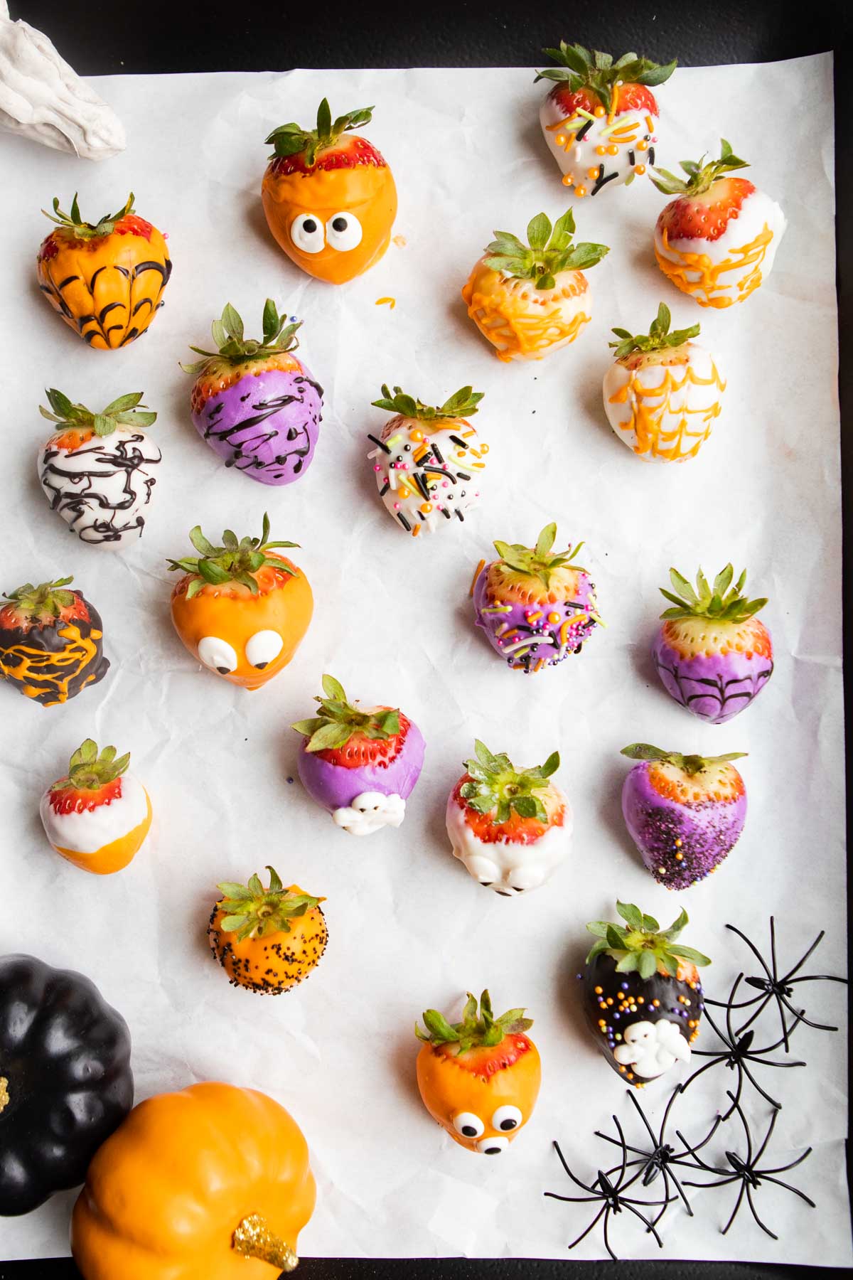 a black tray lined with white parchment paper filled with all different types of Halloween chocolate covered strawberries
