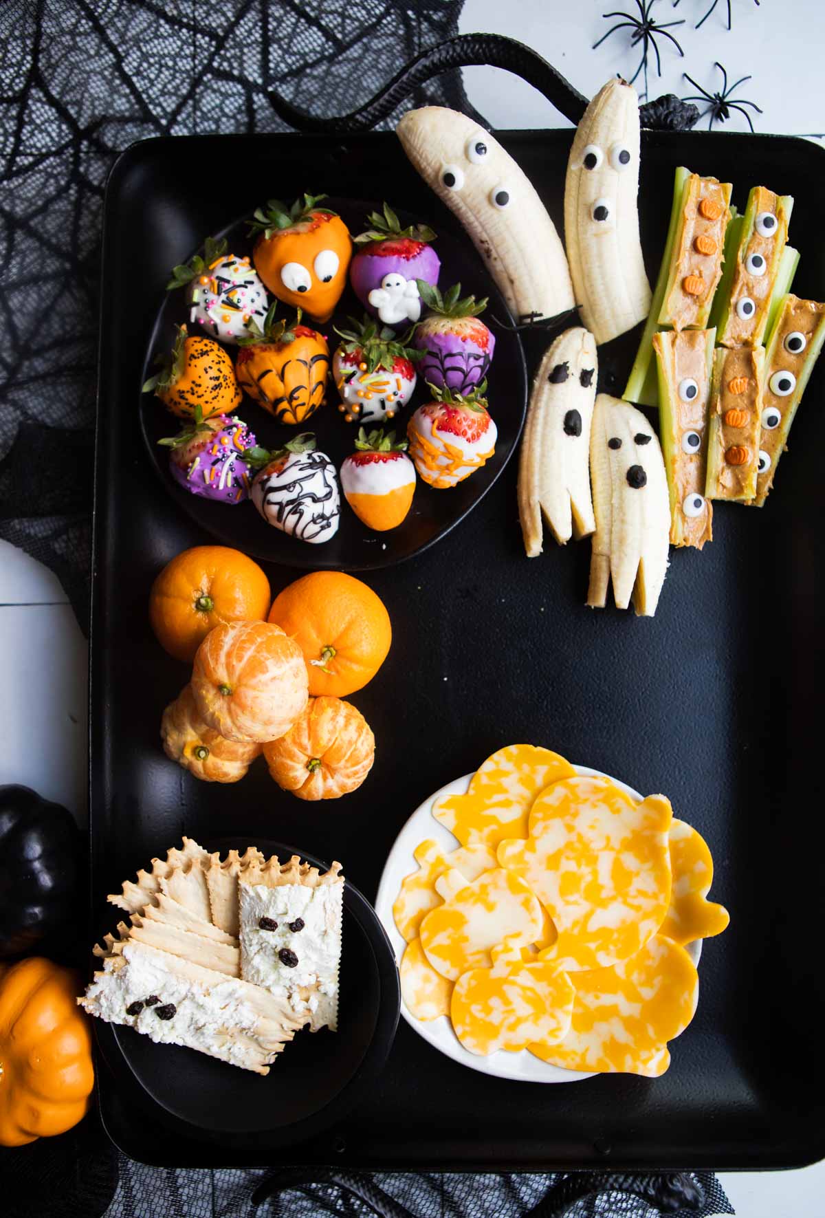 banana ghosts and halloween chocolate covered strawberries on a black snack try