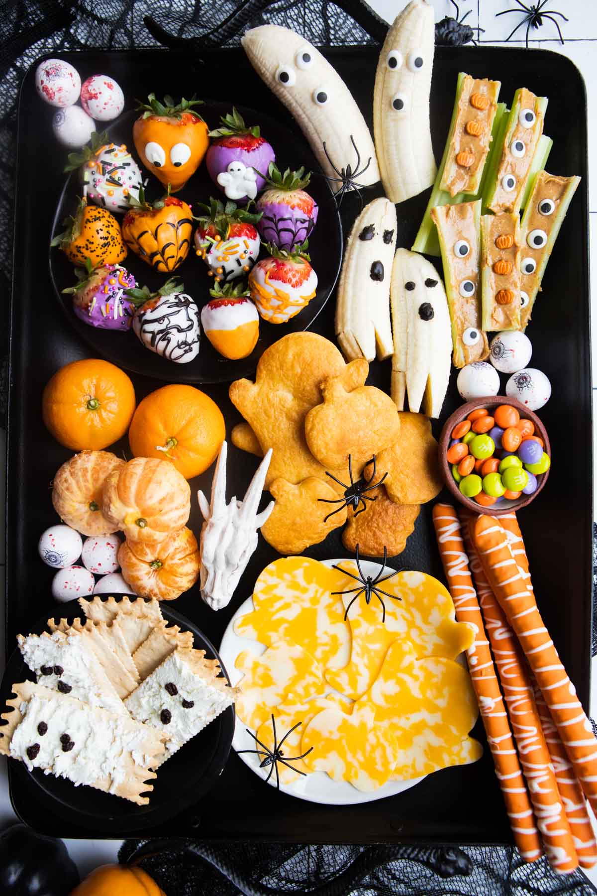 halloween banana ghosts, chocolate covered strawberries, and other halloween snacks on a black metal tray