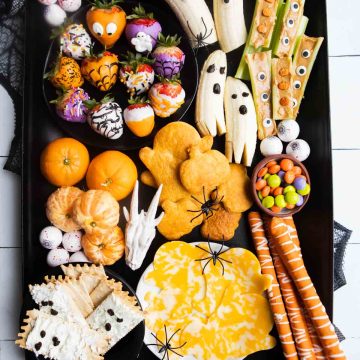 Spooky Halloween snack board made kid-friendly with Halloween candy and treats on a black metal tray