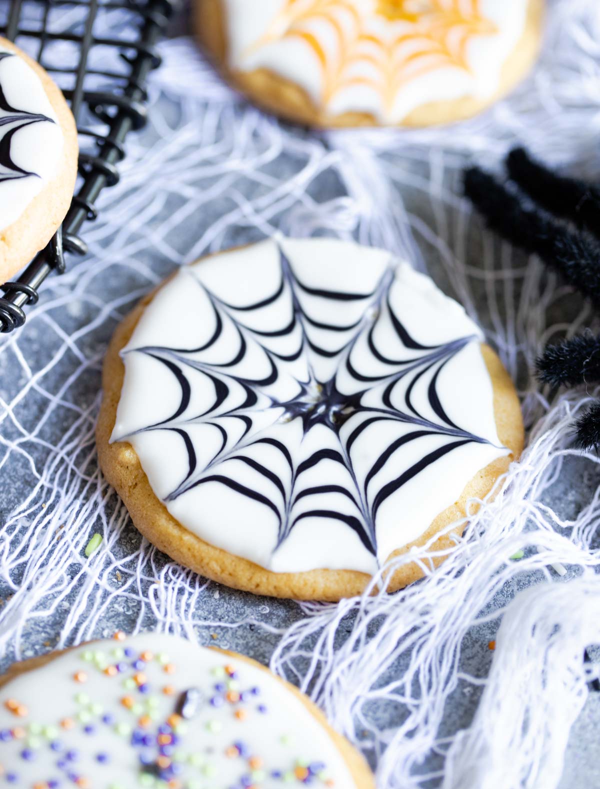 Black and white spider web Halloween sugar cookies on a gray board with white webbing strewn across it