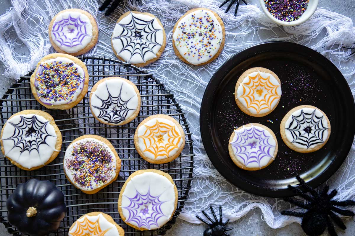 a black plate and cooling rack filled with decorated Halloween sugar cookies