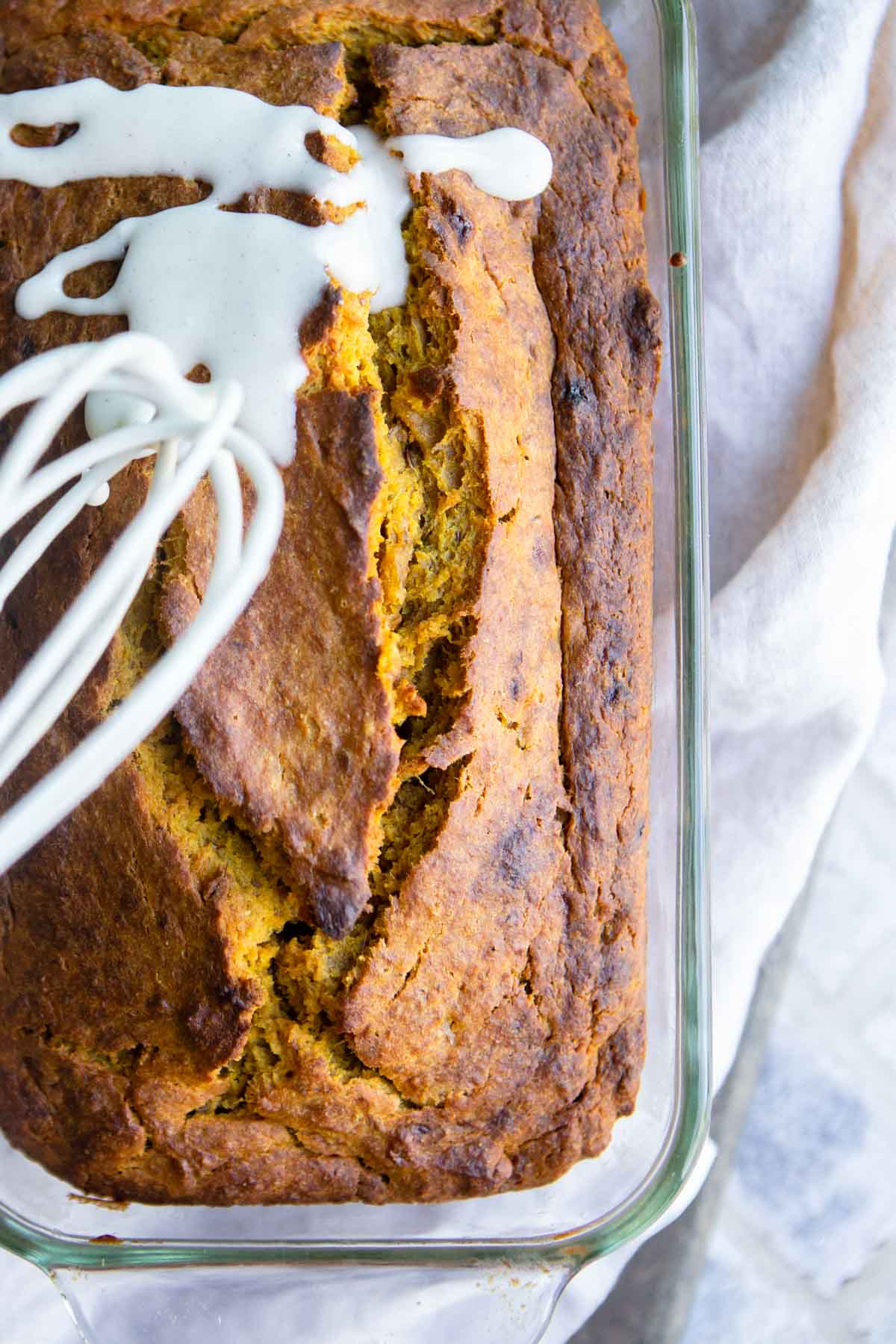 whisk spooning on glaze for pumpkin bread all over a loaf of pumpkin banana bread