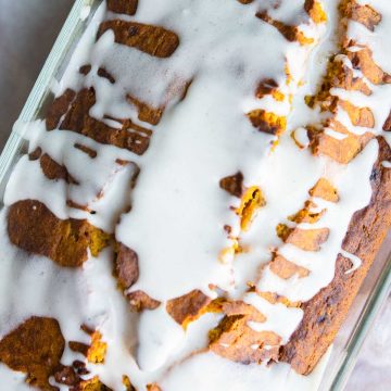 whisk spooning on glaze for pumpkin bread all over a loaf of pumpkin banana bread