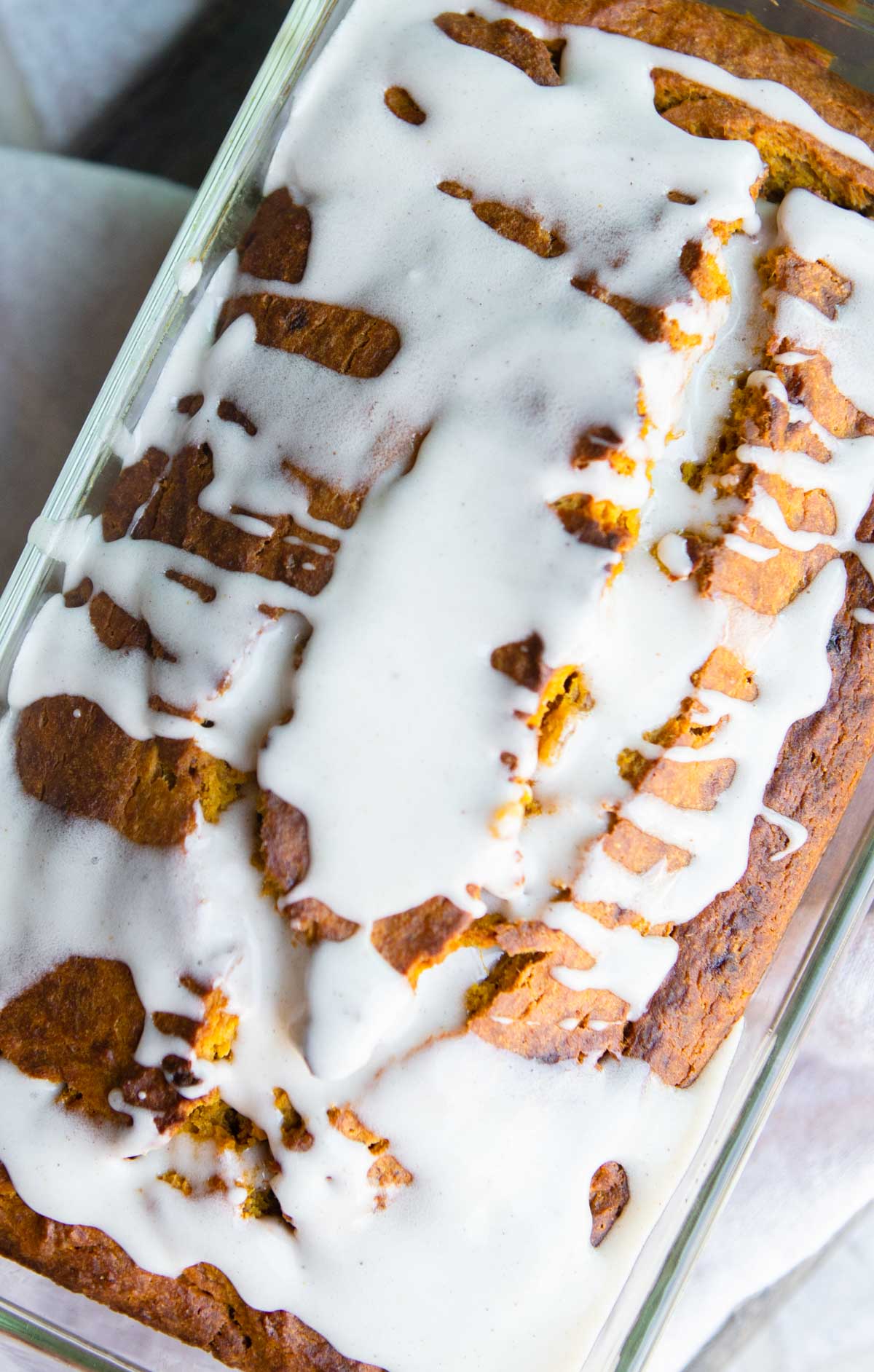 whisk spooning on glaze for pumpkin bread all over a loaf of pumpkin banana bread