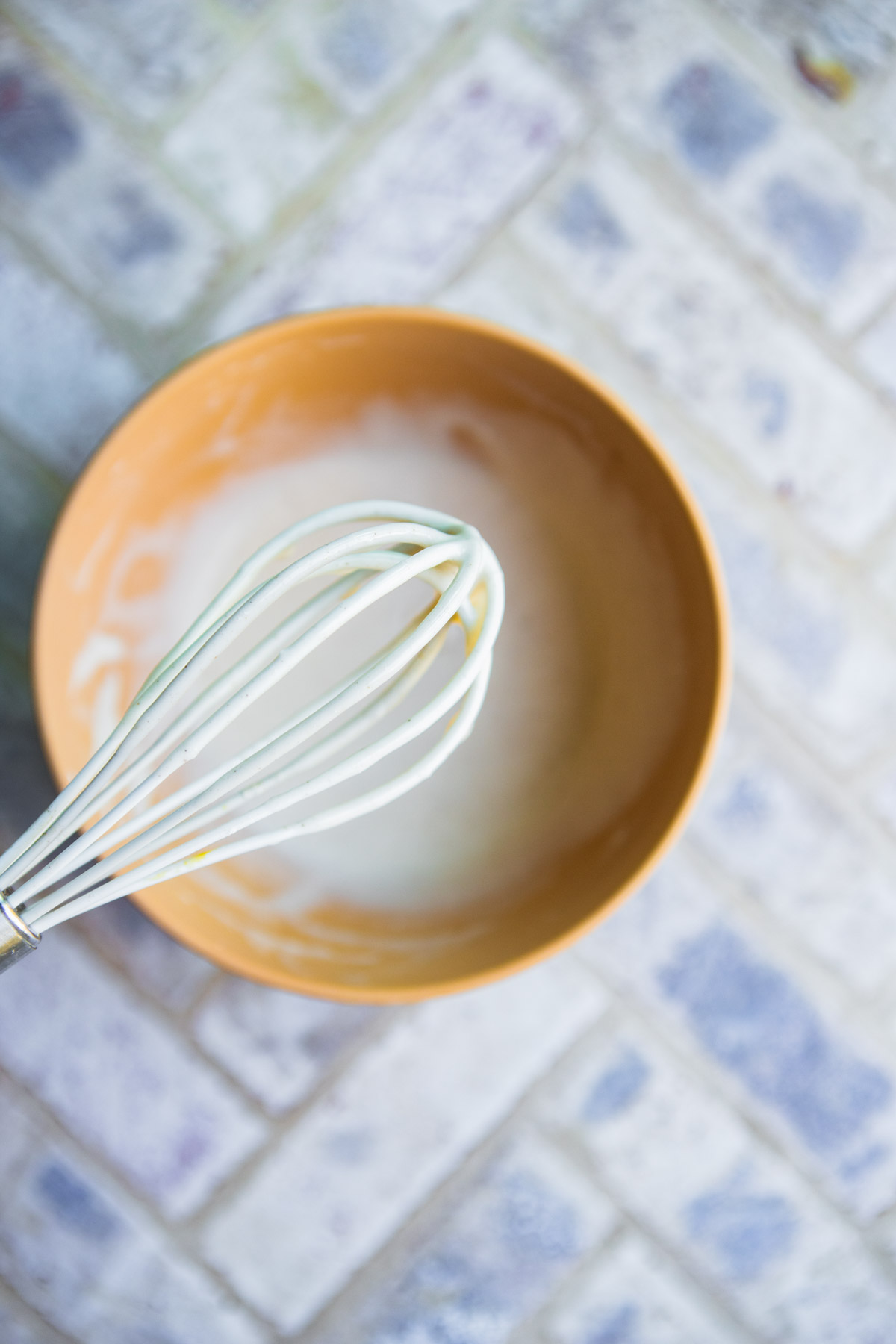 white whisk being dipped in a bowl filled with glaze for pumpkin bread
