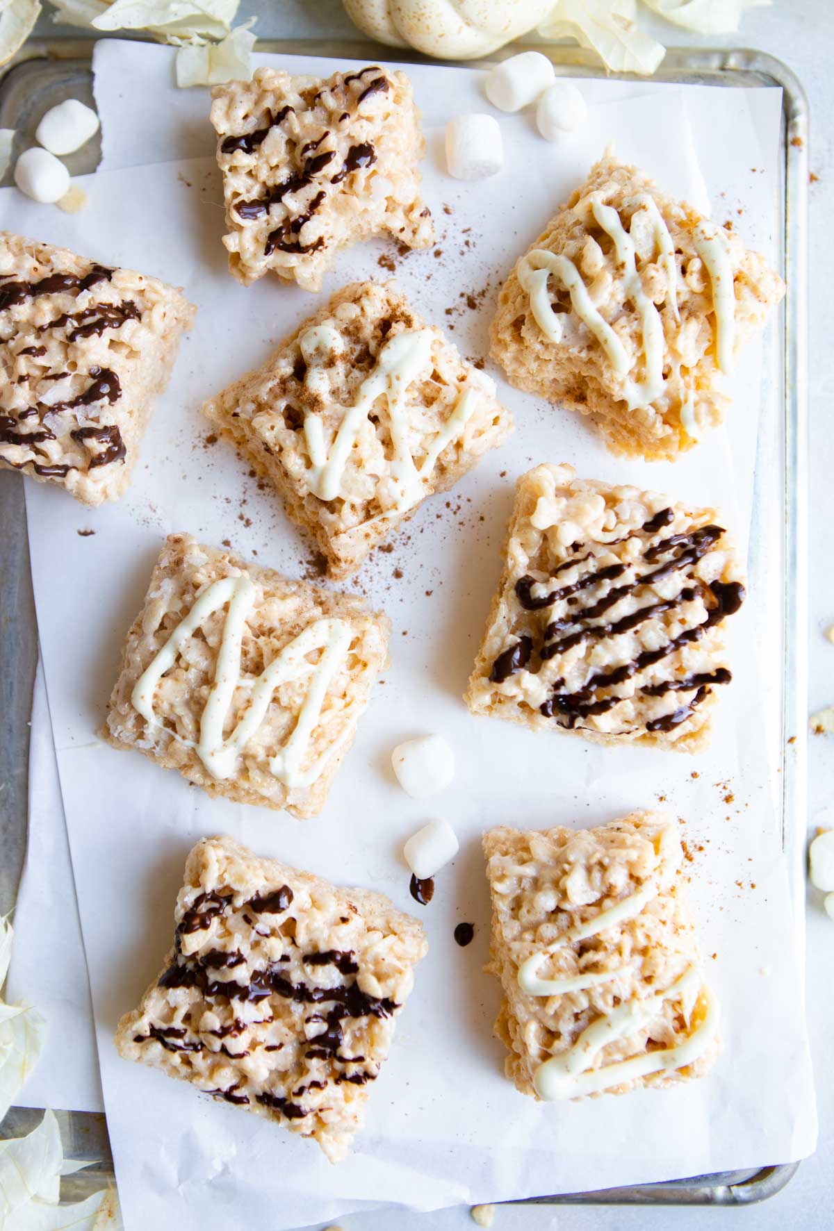 pumpkin rice krispie treats drizzled with melted chocolate on a white piece of parchment paper