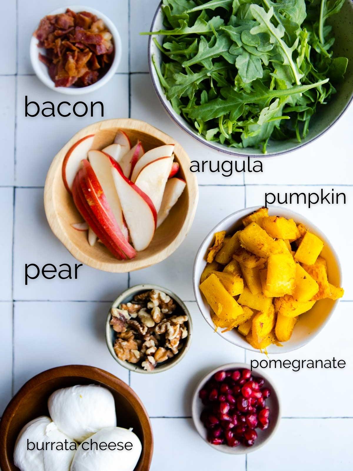 roasted pumpkin, sliced bacon, sliced pear, burrata, pomegranate seeds and walnuts and arugula in small round bowls ready to make a salad