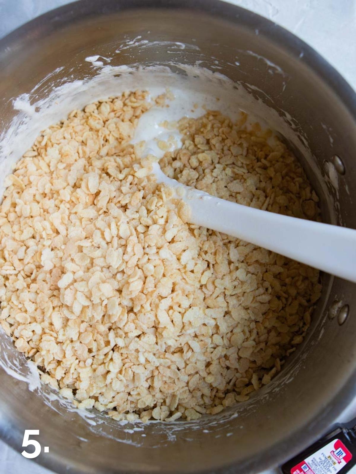 rice krispie cereal being stirred into a big pot of melted butter and marshmallows