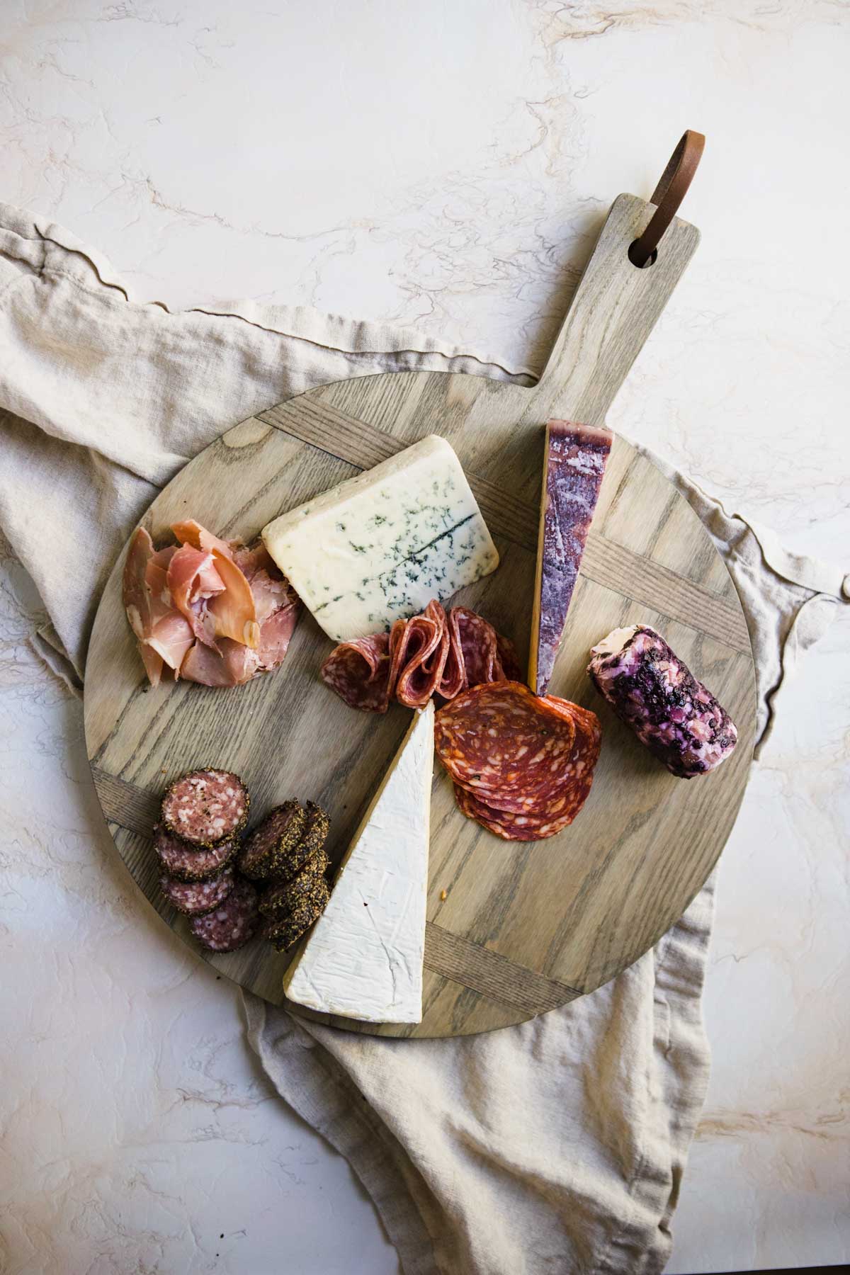 round wooden board filled with hard and soft cheese and cured meats