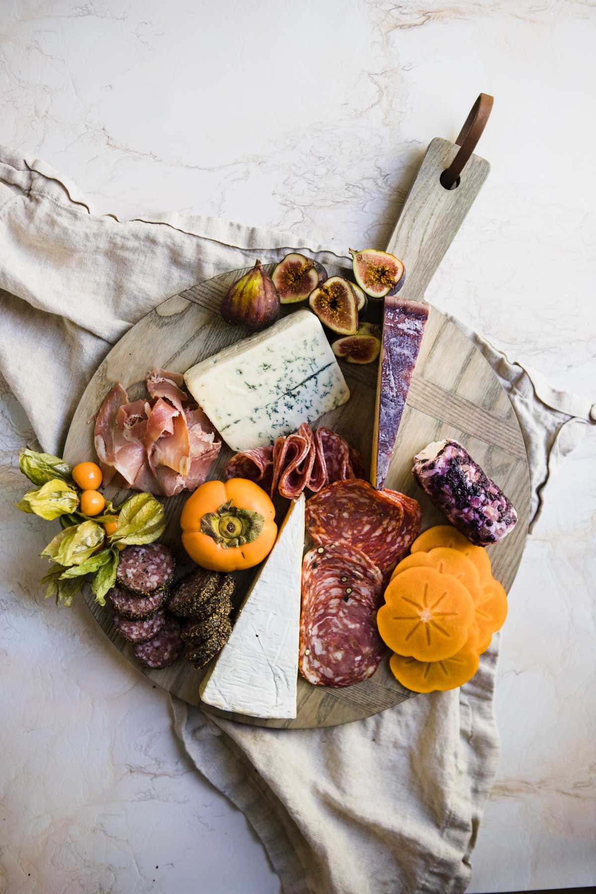 seasonal fruits like figs and persimmons and goldenberries are added to a Fall themed charcuterie board 