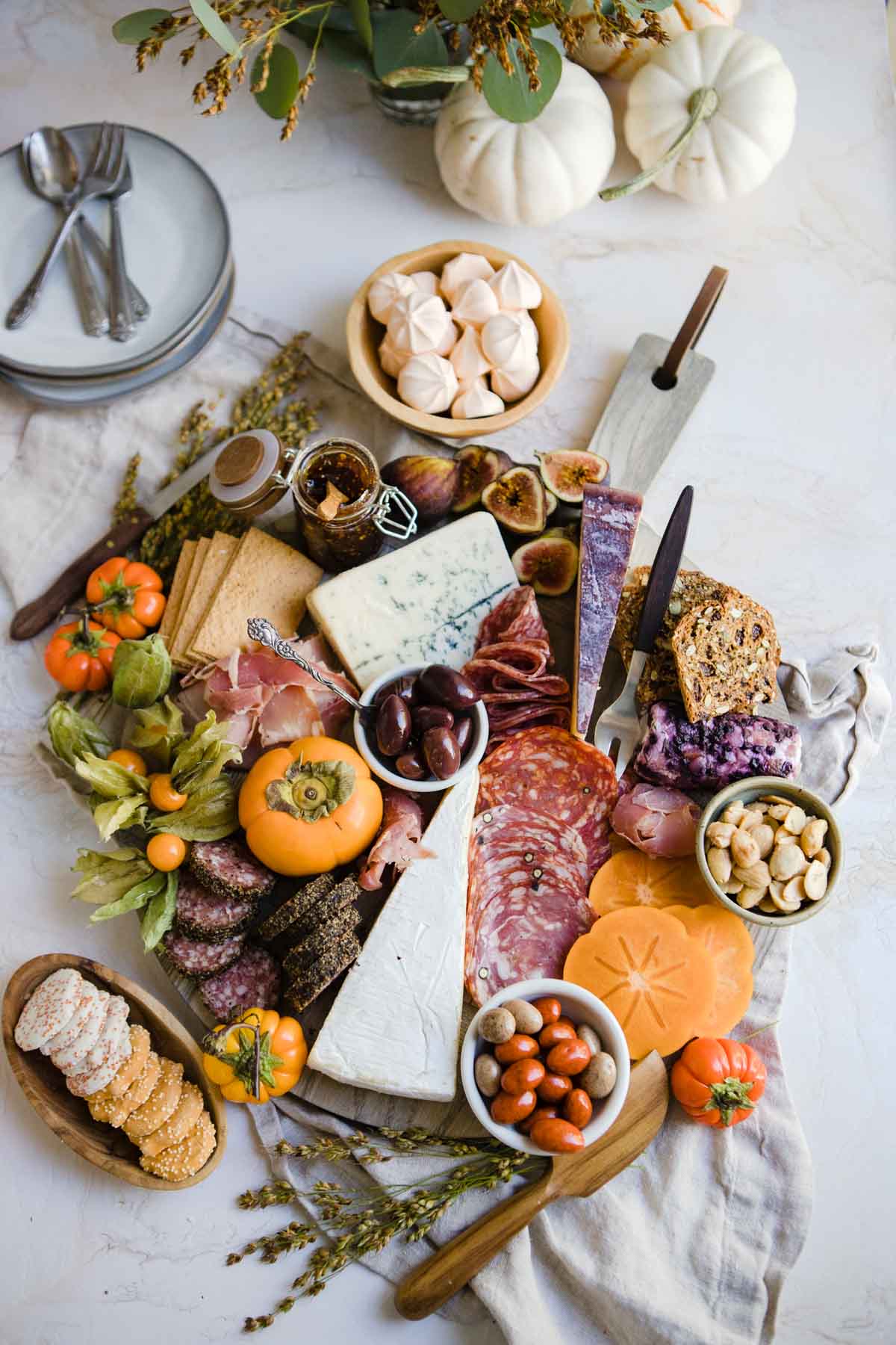 A large charcuterie board made for the Fall season with orange persimmons, figs and mini fresh pumpkins 