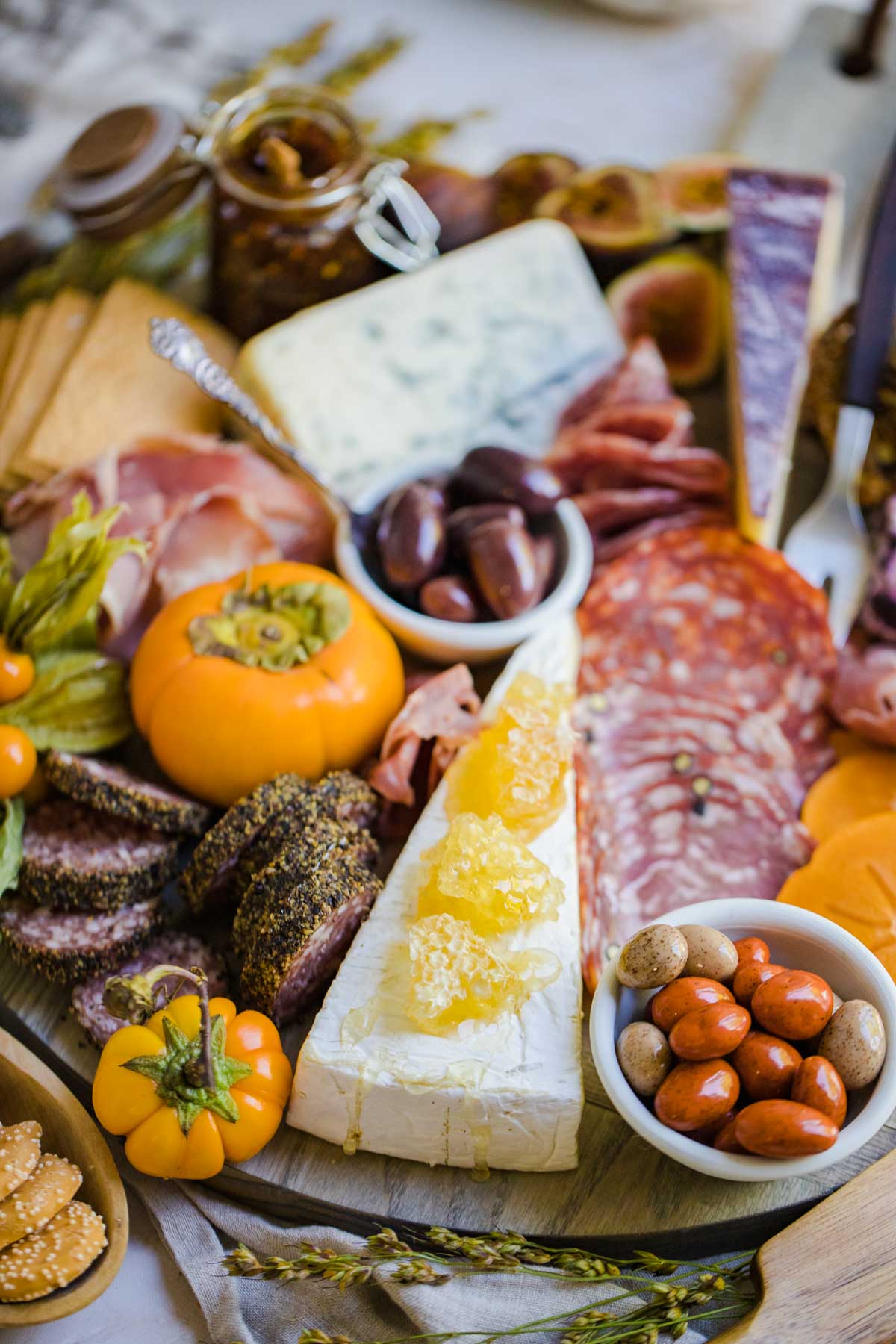persimmons, brie cheese covered with honeycomb, salami and nuts all spread out on a round wooden board