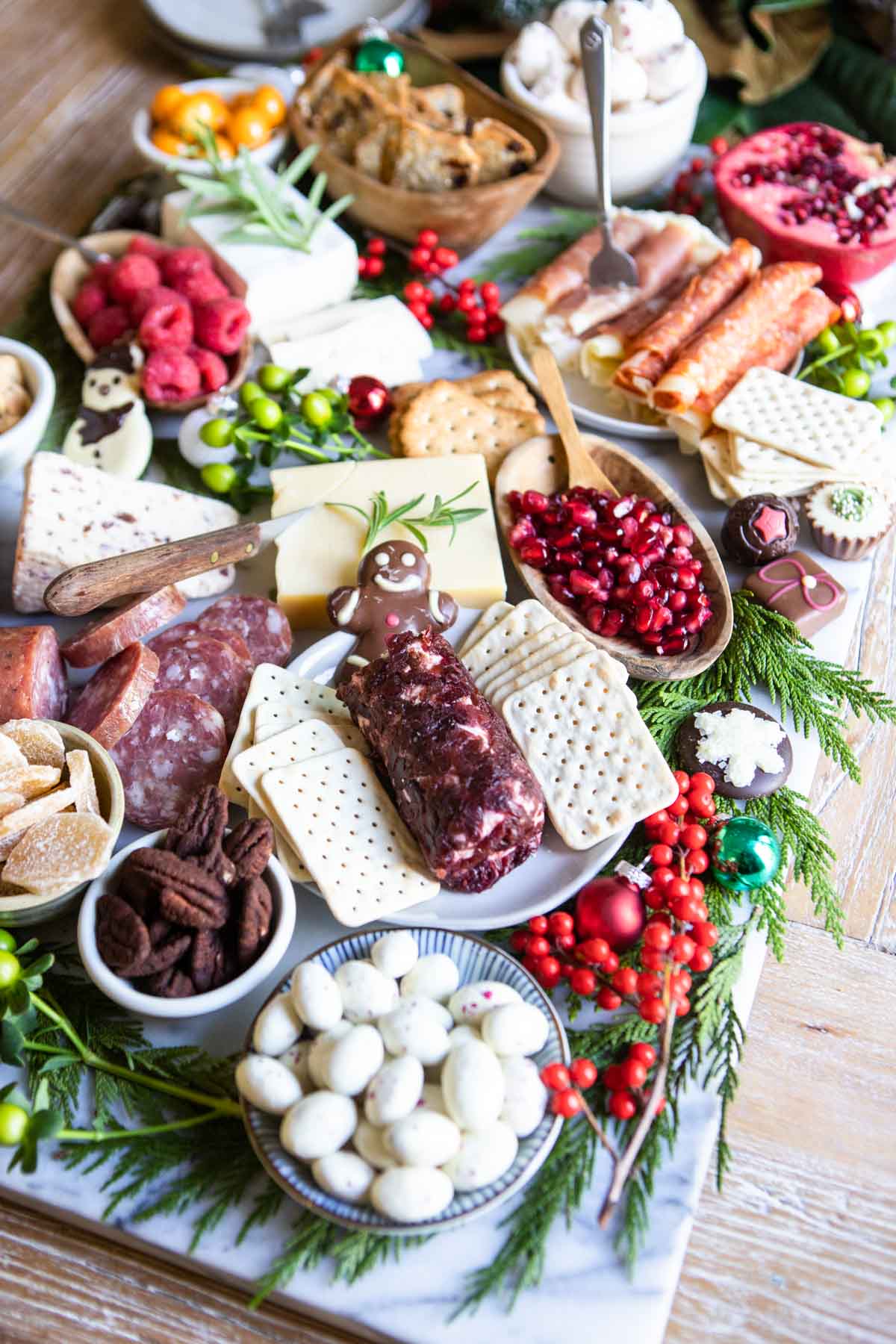 Christmas charcuterie board on a marble platter made with red and green decorative items and nuts and cheeses