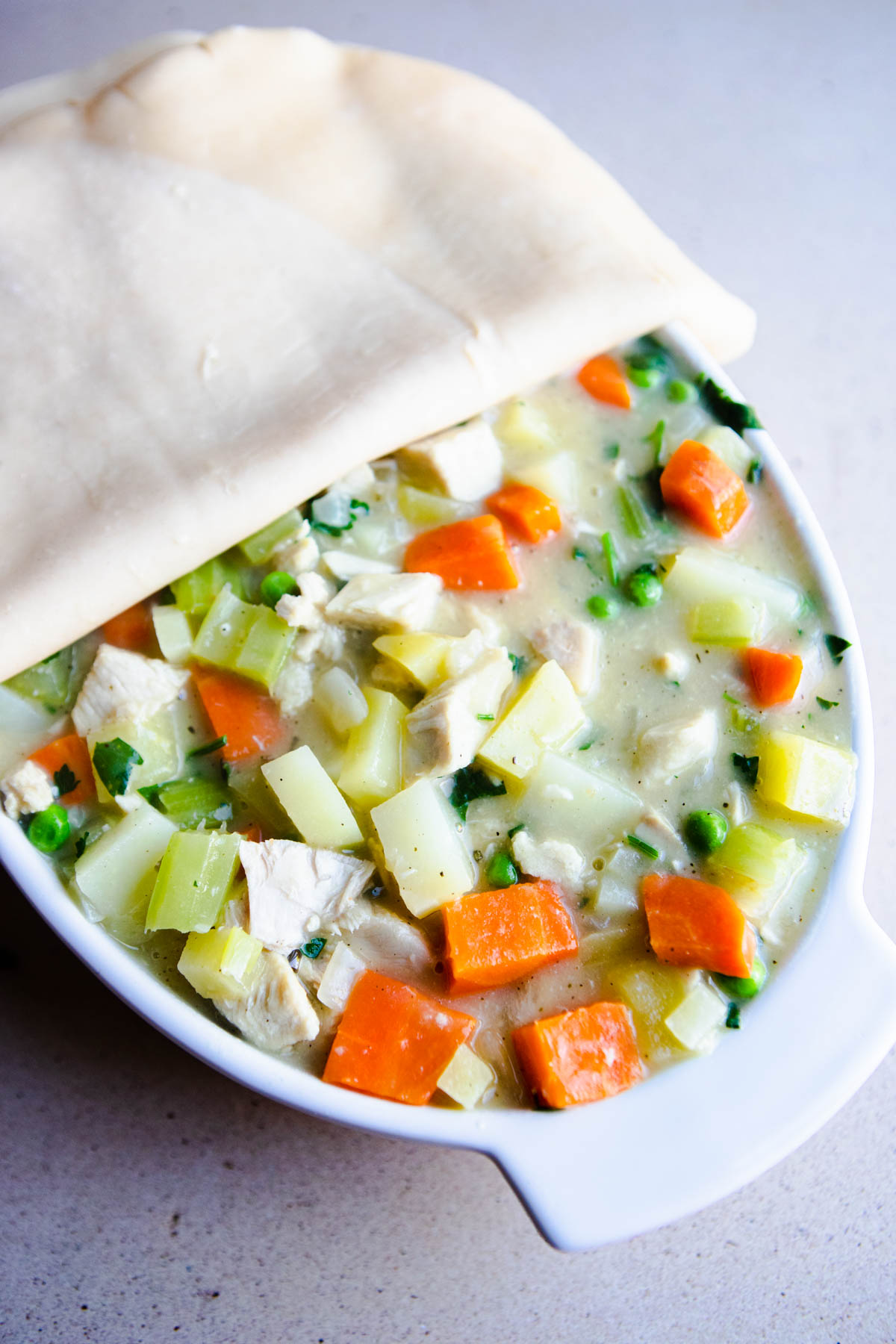 pot pie filling in a casserole dish being covered with a pie crust