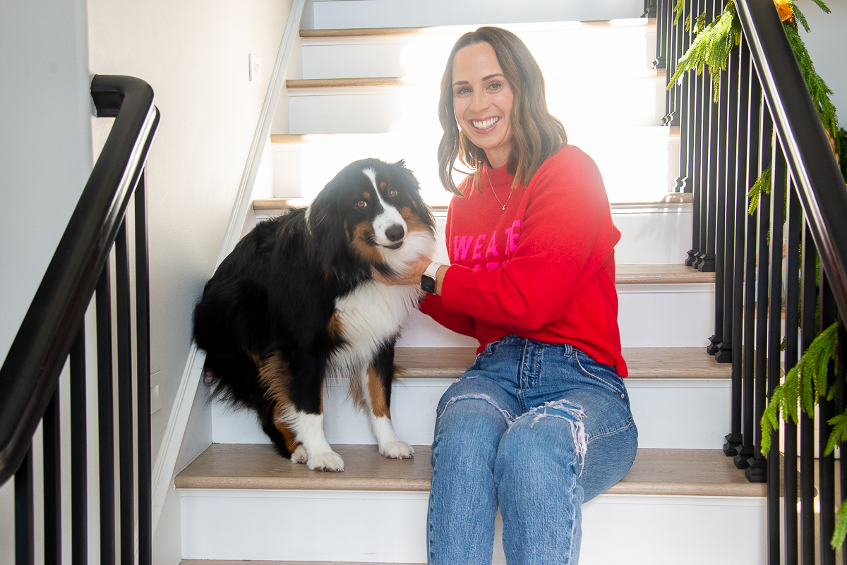 women in red sweater and jeans sitting on stairs with a tri-color Australian Shepard dog 