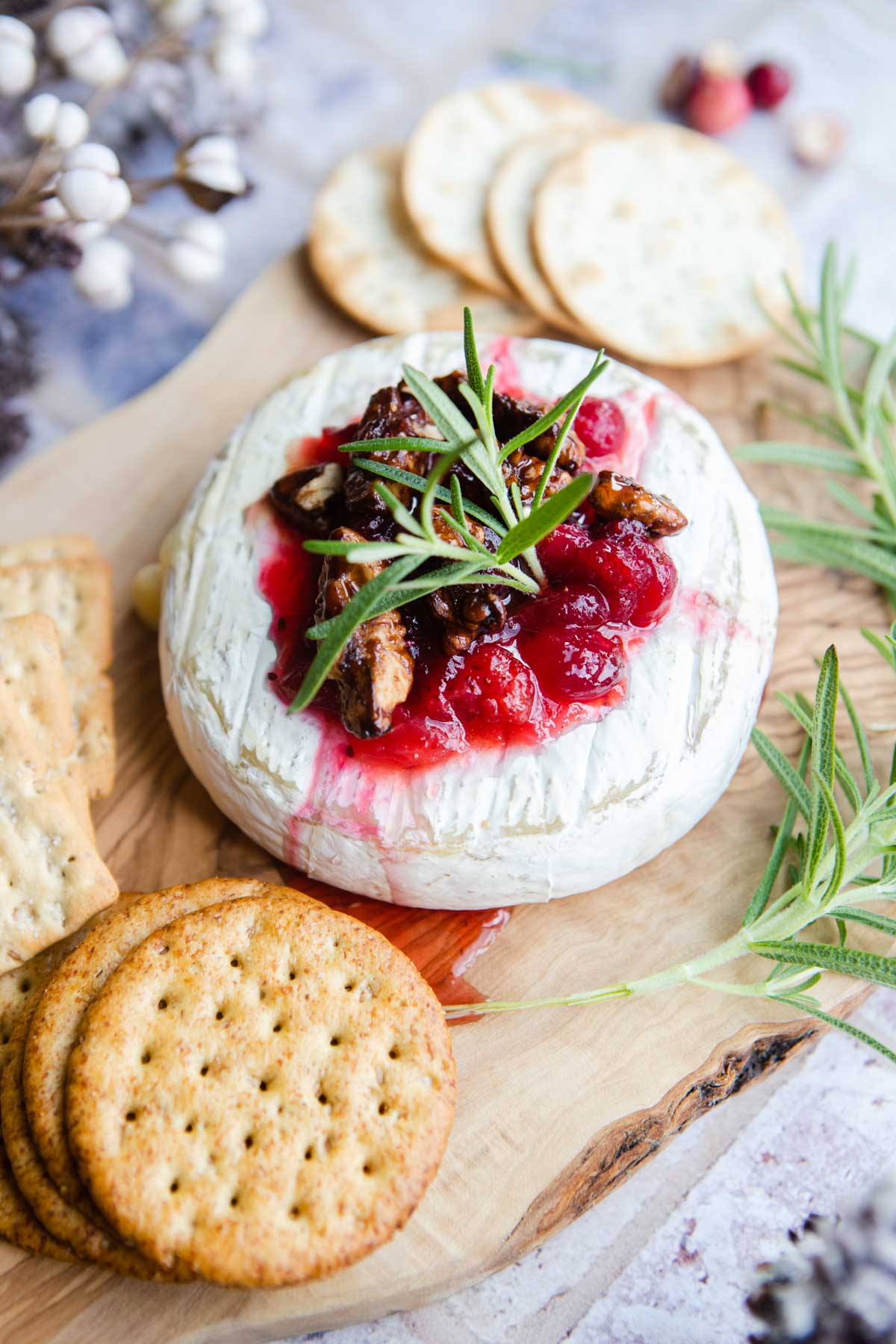 wheel of brie on a wood board topped with cranberry jam and surrounded by crackers