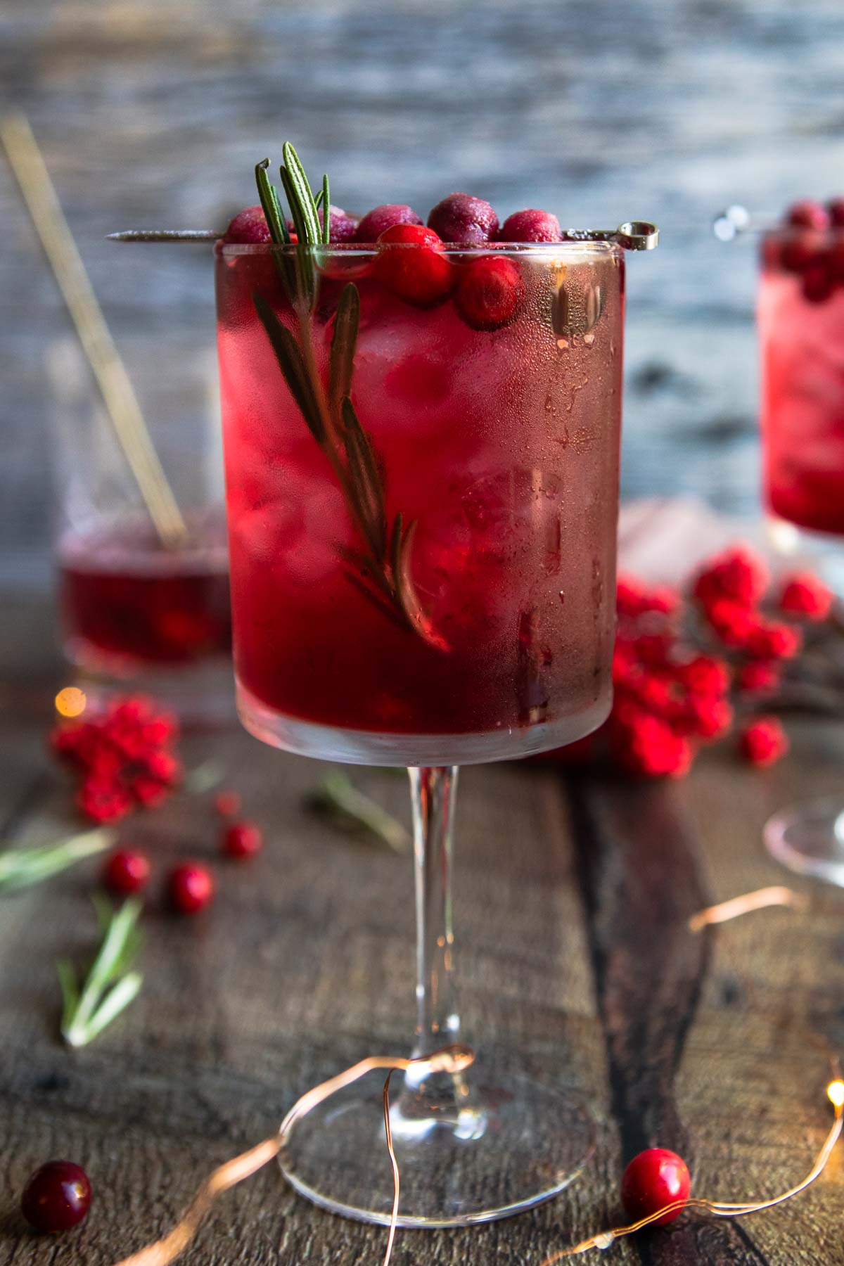 pink gin spritz in a tall wine glass garnished with cranberries and rosemary