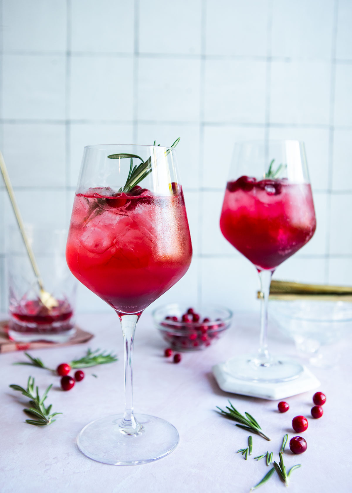 cranberry St Germain spritz in tall wine glasses garnished with rosemary and cranberries 