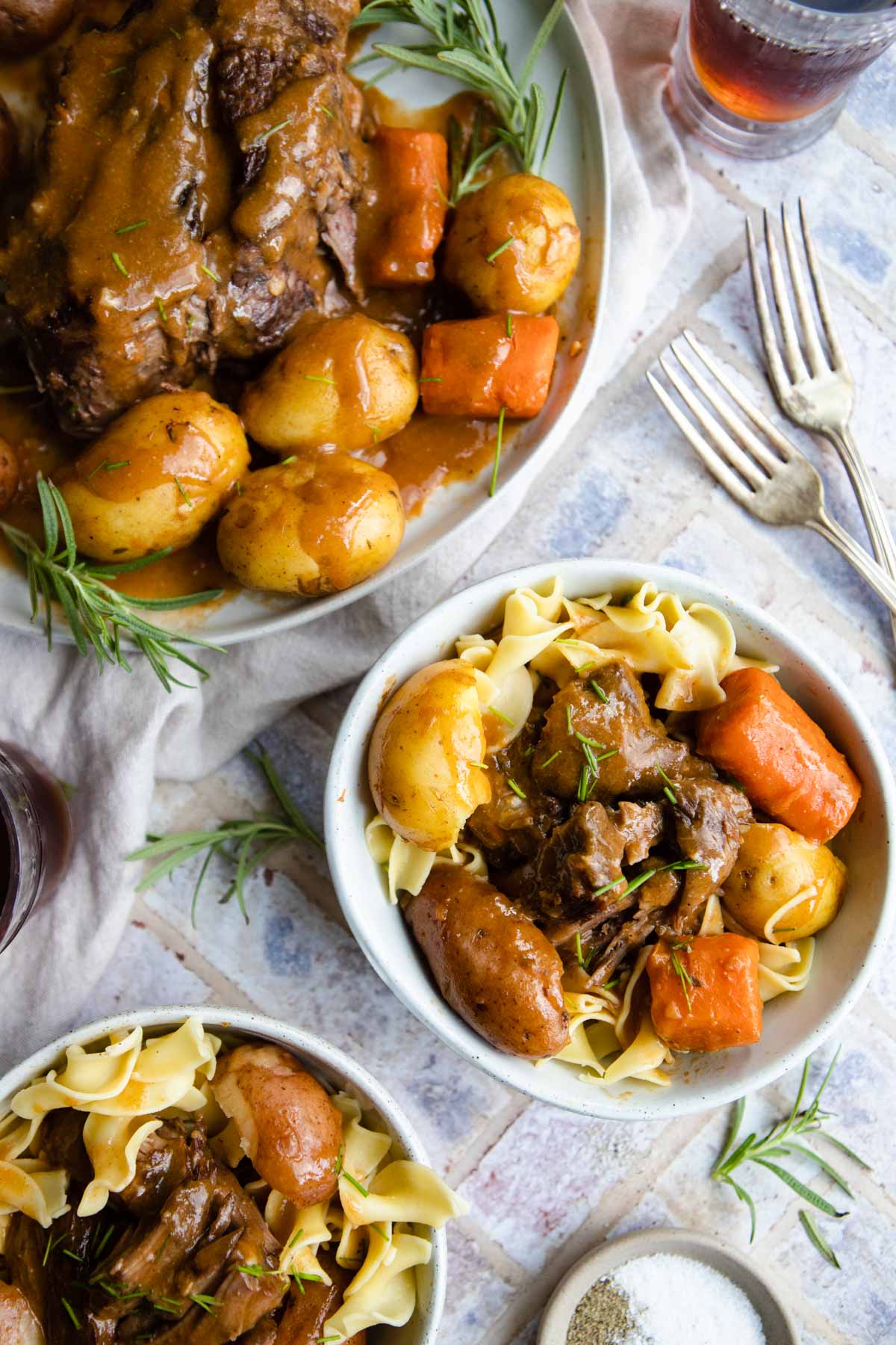 beef pot roast and gravy on a platter and in bowls with egg noodles