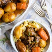 old fashioned pot roast with carrots and potatoes on a bed of buttered egg noodles