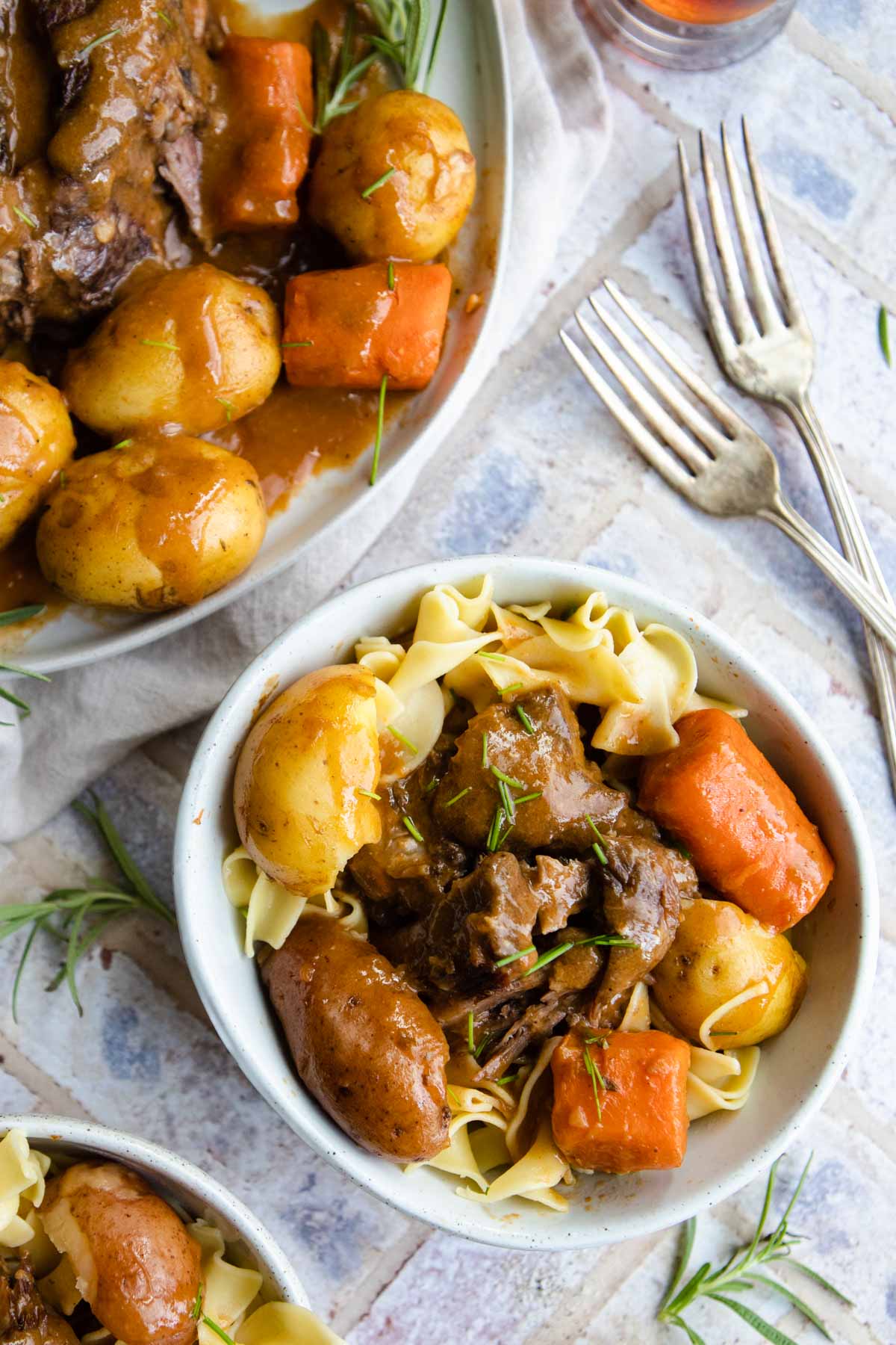 old fashioned pot roast with carrots and potatoes on a bed of buttered egg noodles