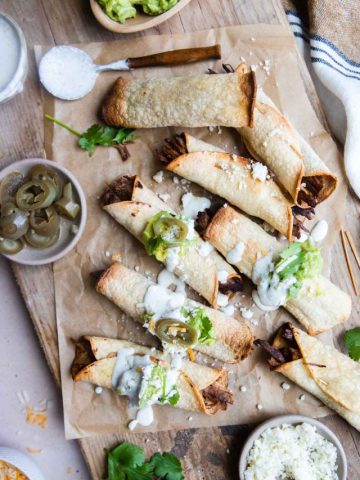 shredded beef air fryer taquitos on a board and garnished with various toppings