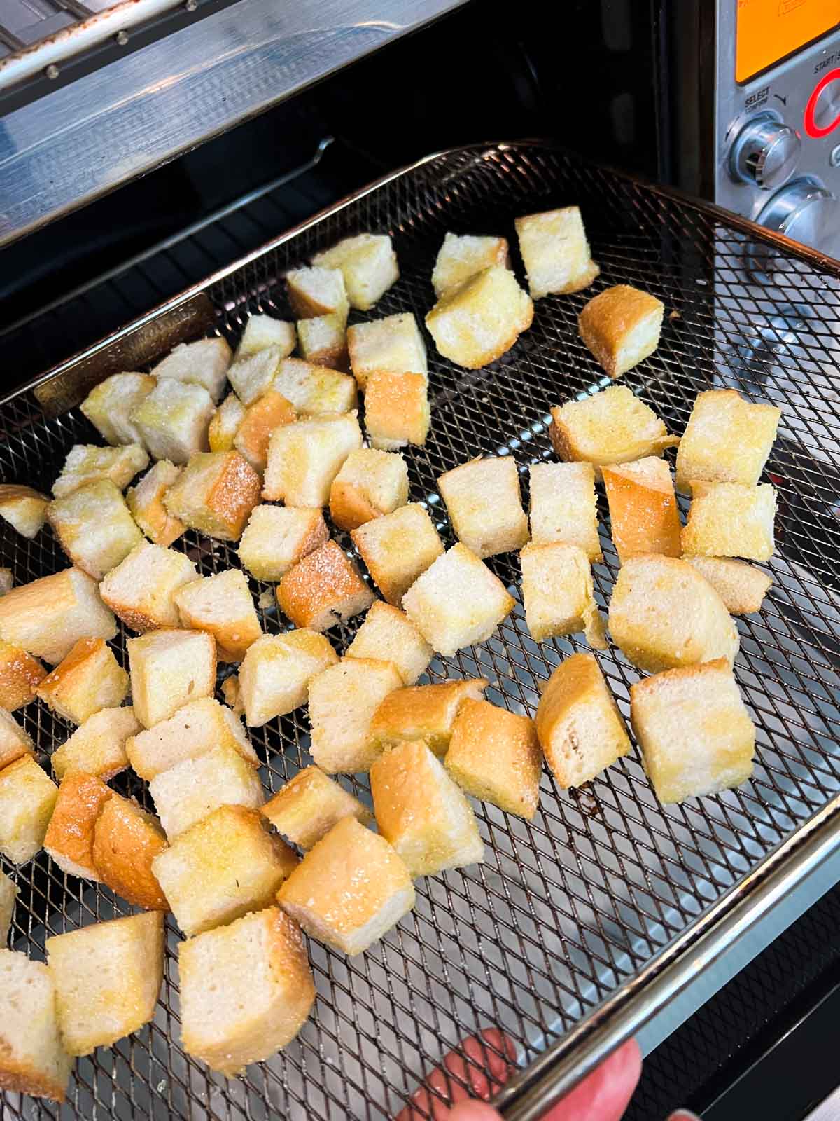 cubed bread spread out on an air fryer basket tray
