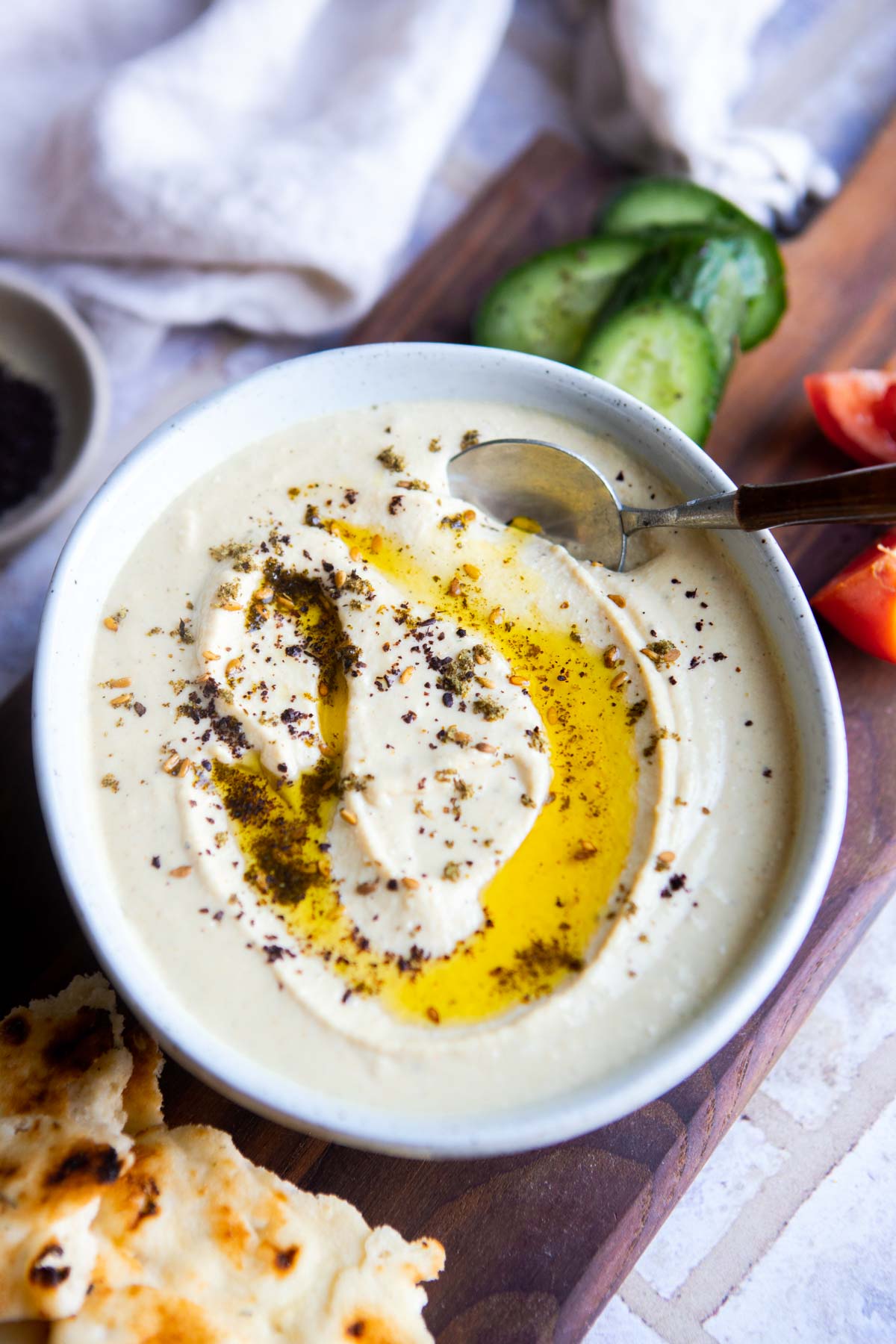 cream bowl filled with homemade hummus dip next to pita bread and fresh veggies 