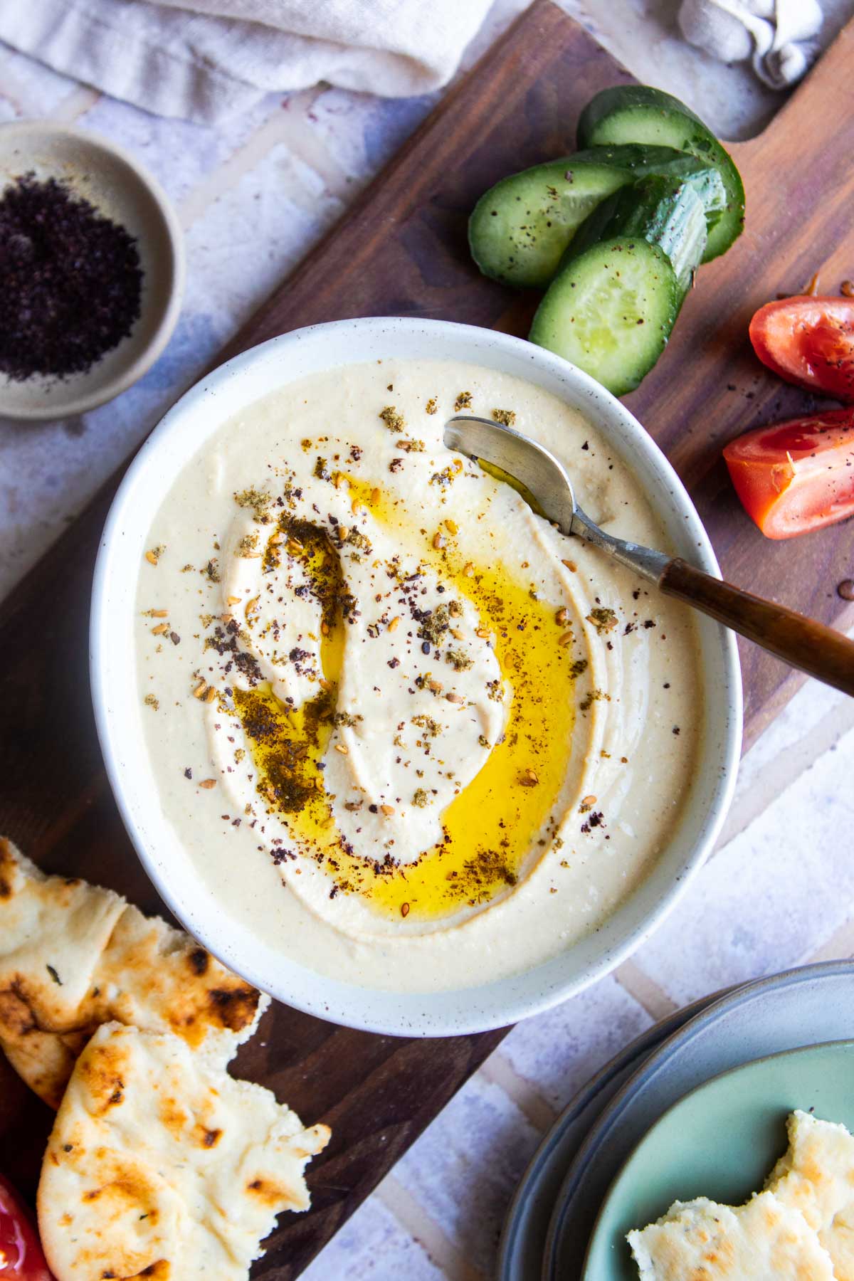 wood spoon in a bowl of protein hummus with olive oil and sumac sprinkled on top 