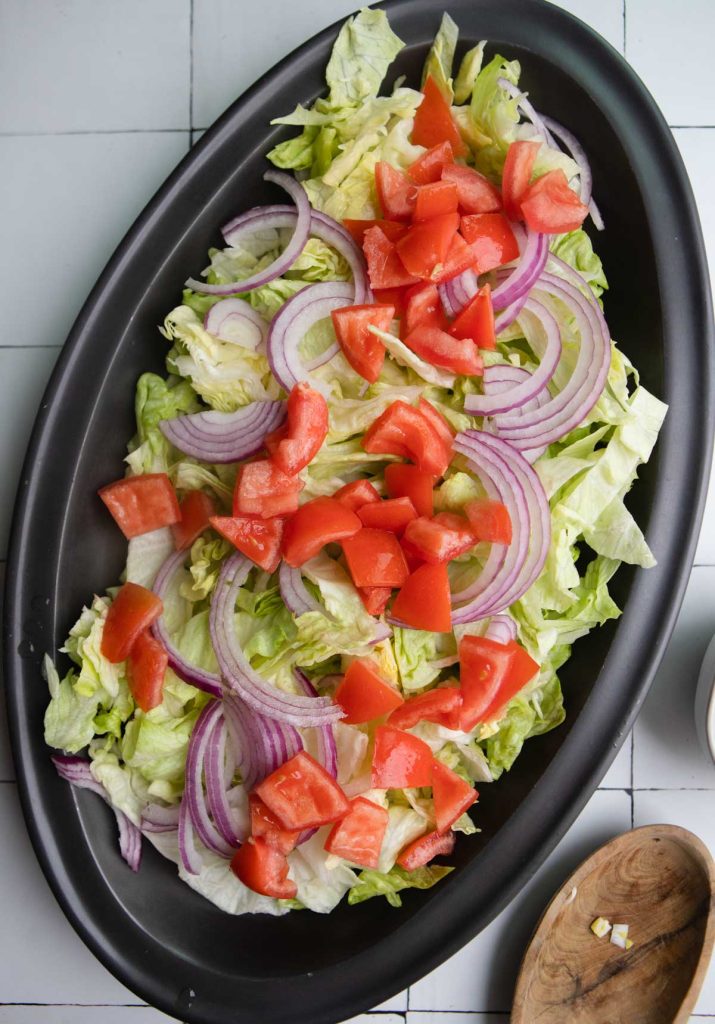 sliced red onions, tomatoes and iceberg lettuce on a black platter
