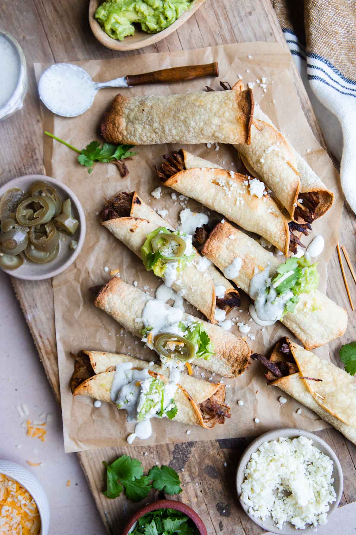 shredded beef air fryer taquitos on a board and garnished with various toppings 