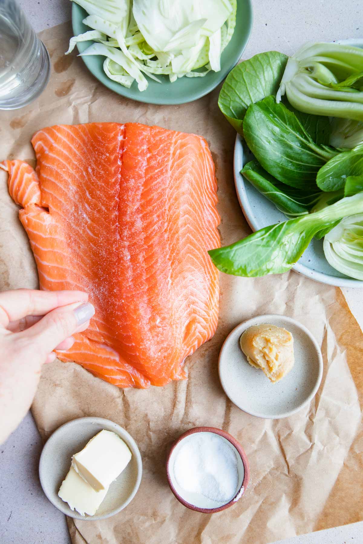 women sprinkling salt on a large filet of salmon 