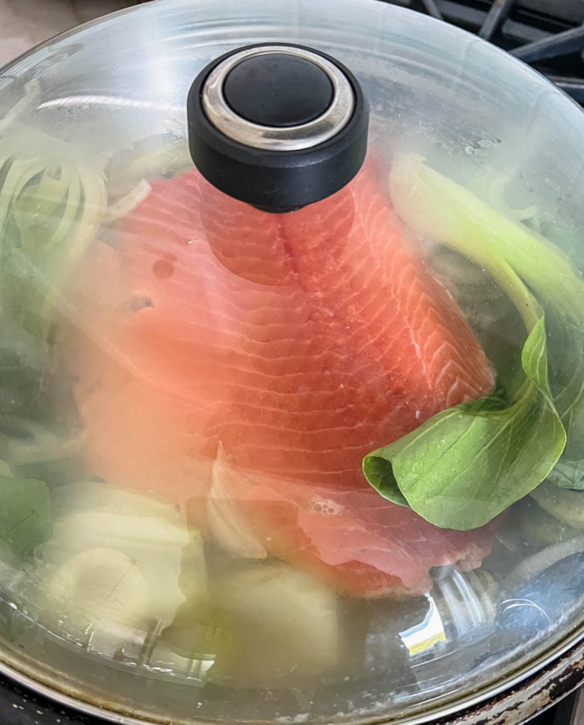 lid being placed on a large skillet filled with salmon and veggies