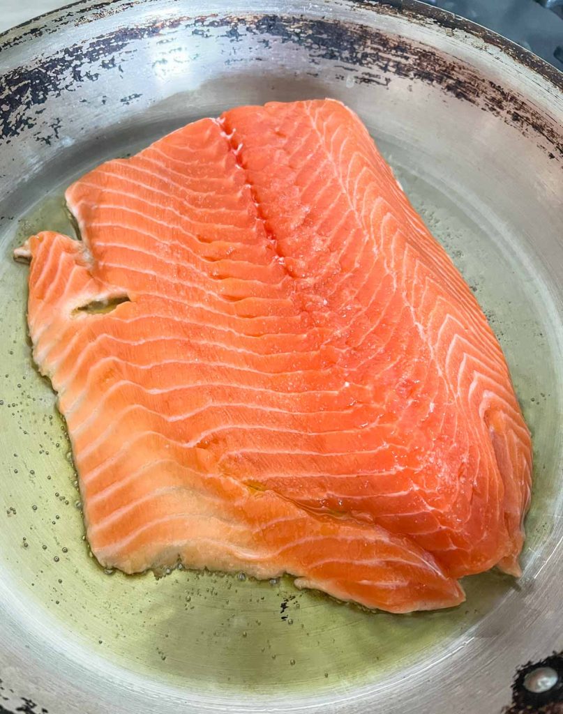 raw salmon in a large skillet set on medium-low heat