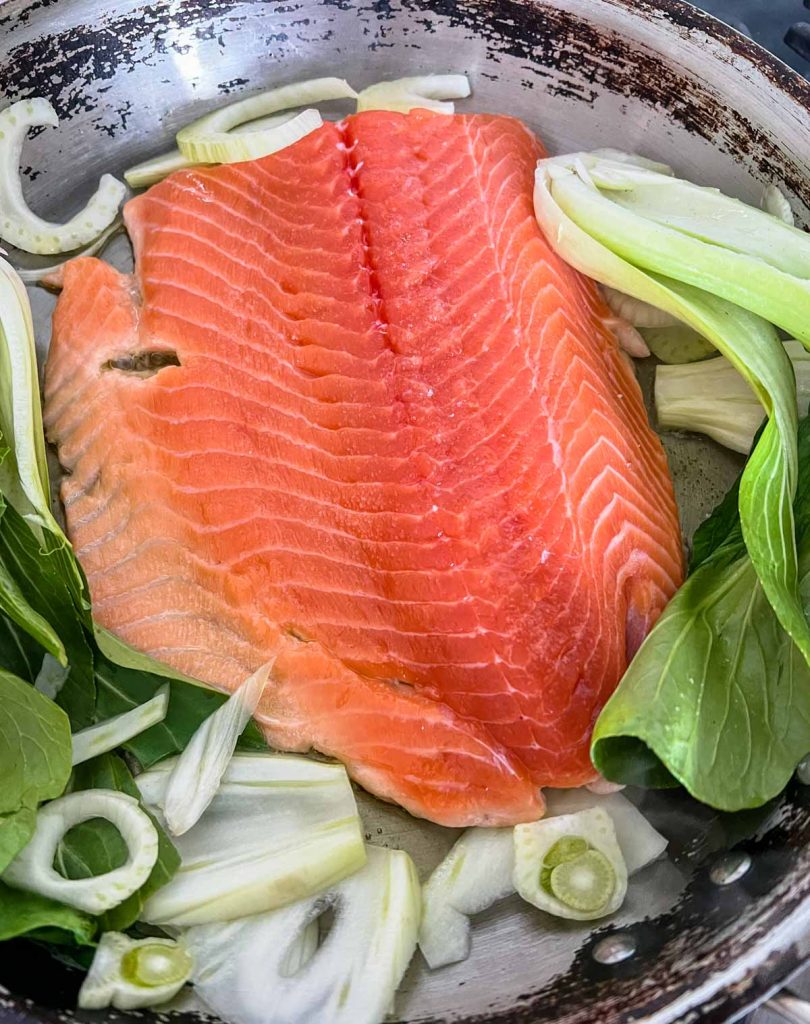raw salmon filet and baby bok choy and fennel in a large skillet