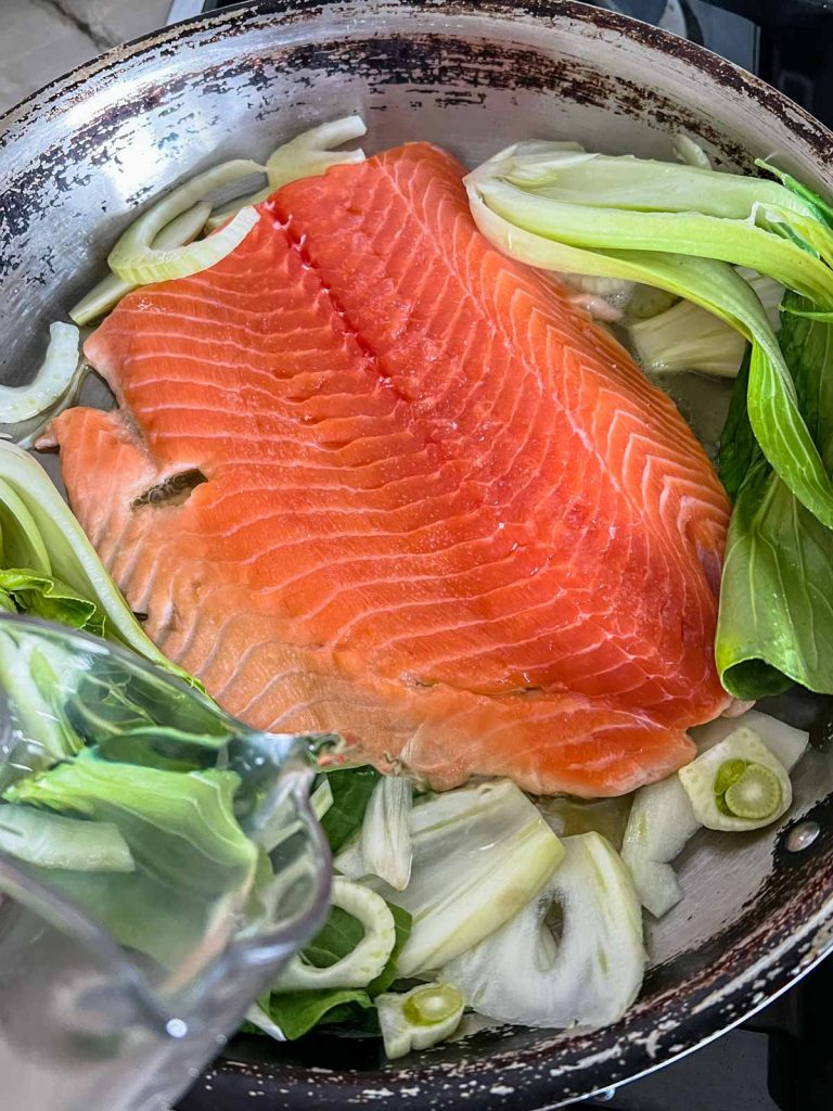 dry white wine being added to a skillet filled with salmon filet and baby bok choy