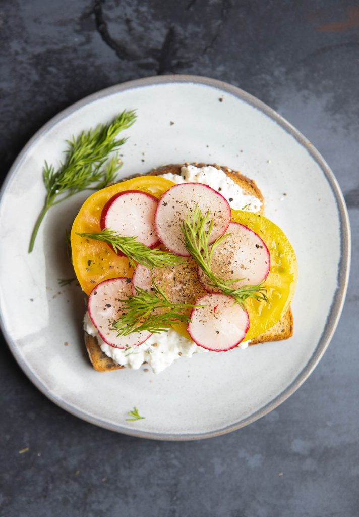 sliced tomatoes and radishes on cottage cheese toast with fresh dill and cracked black pepper